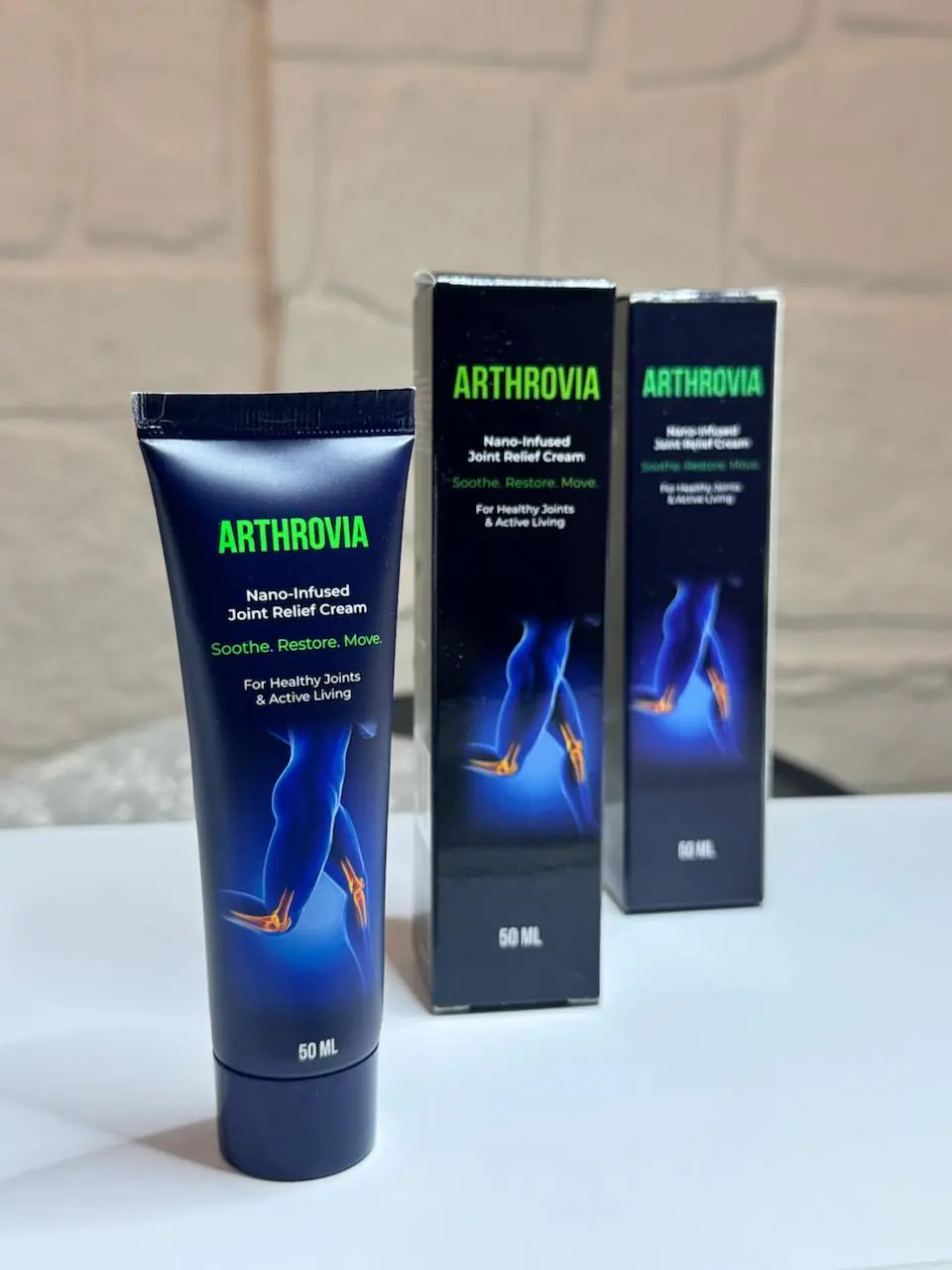 Tuba Arthrovia 50 ml in dve škatli na beli mizi pred kamnito steno